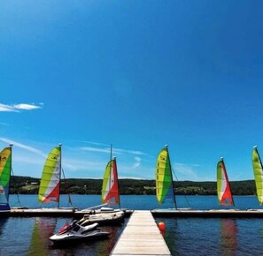 A dock with several sailboats and a jet ski, a clear blue sky, and a calm lake.