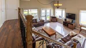 A spacious living room with a large sectional sofa, a wooden coffee table, and a television. - Domaine Bleu - Lakefront & Private Beach (Pohénégamook)