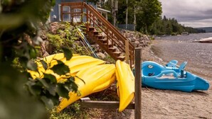 A wooden staircase leading to a house, a yellow kayak, and a blue kayak on a sandy beach. - Domaine Bleu - Lakefront & Private Beach (Pohénégamook)