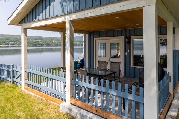 A covered porch with a table and chairs, overlooking a lake.
