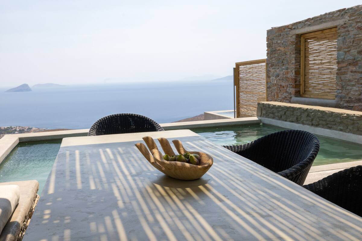 A table with a bowl of fruit, a pool, and a view of the sea.