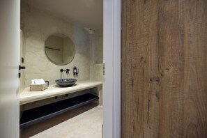 Une salle de bain avec un miroir rond, un lavabo et un panier à serviettes.