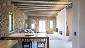 A spacious dining area with a wooden table and chairs, stone walls, and a hanging light fixture. - Kalma Living - Luxury Villas (Kithnos)