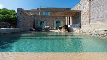 A stone building with a pool, outdoor seating, and a clear blue sky.