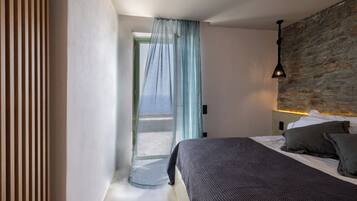 A bedroom with a bed, a window with sheer curtains, a stone wall, and a hanging light fixture.