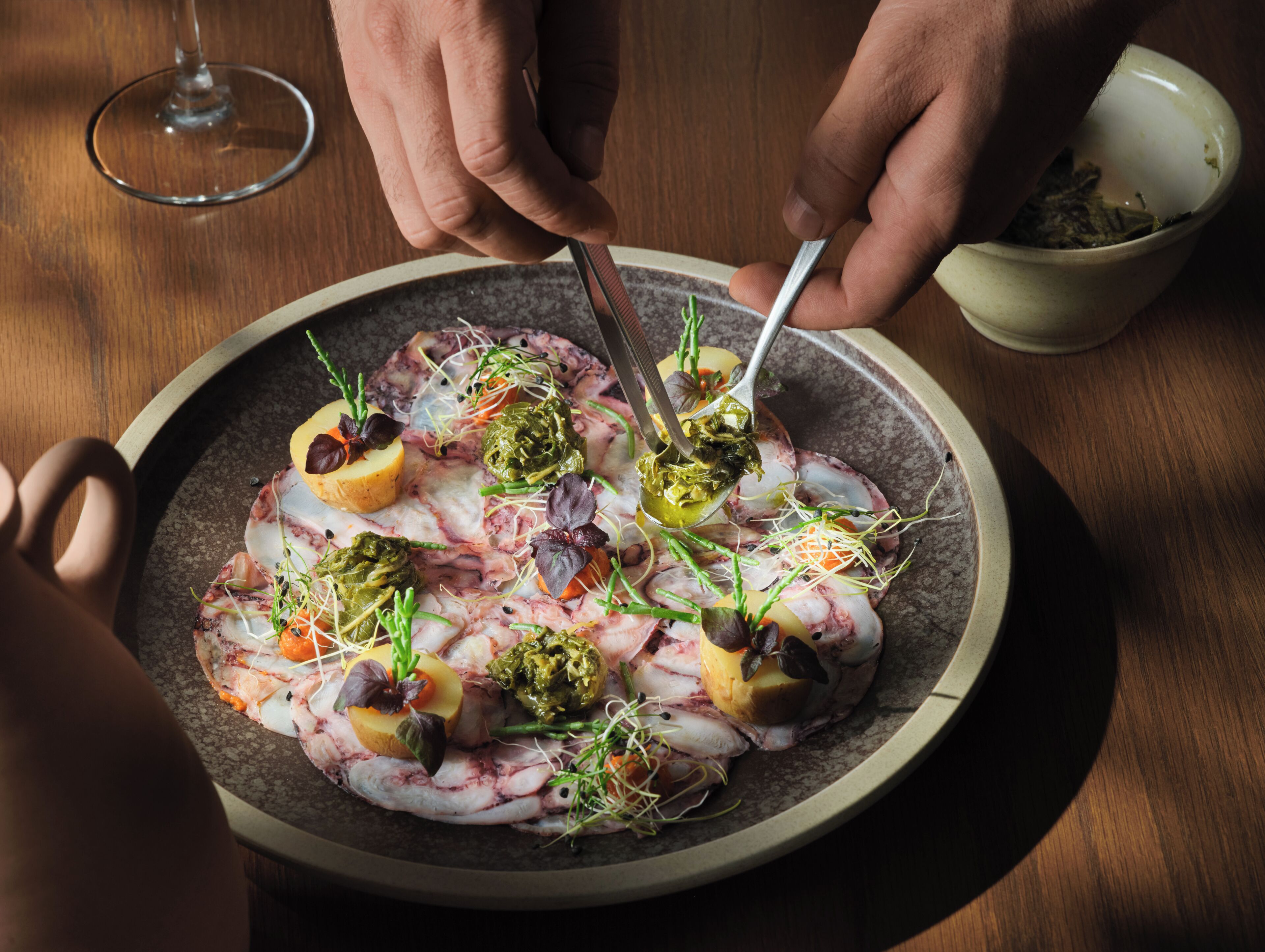 A plate of food with various garnishes and a glass of wine on a wooden table.