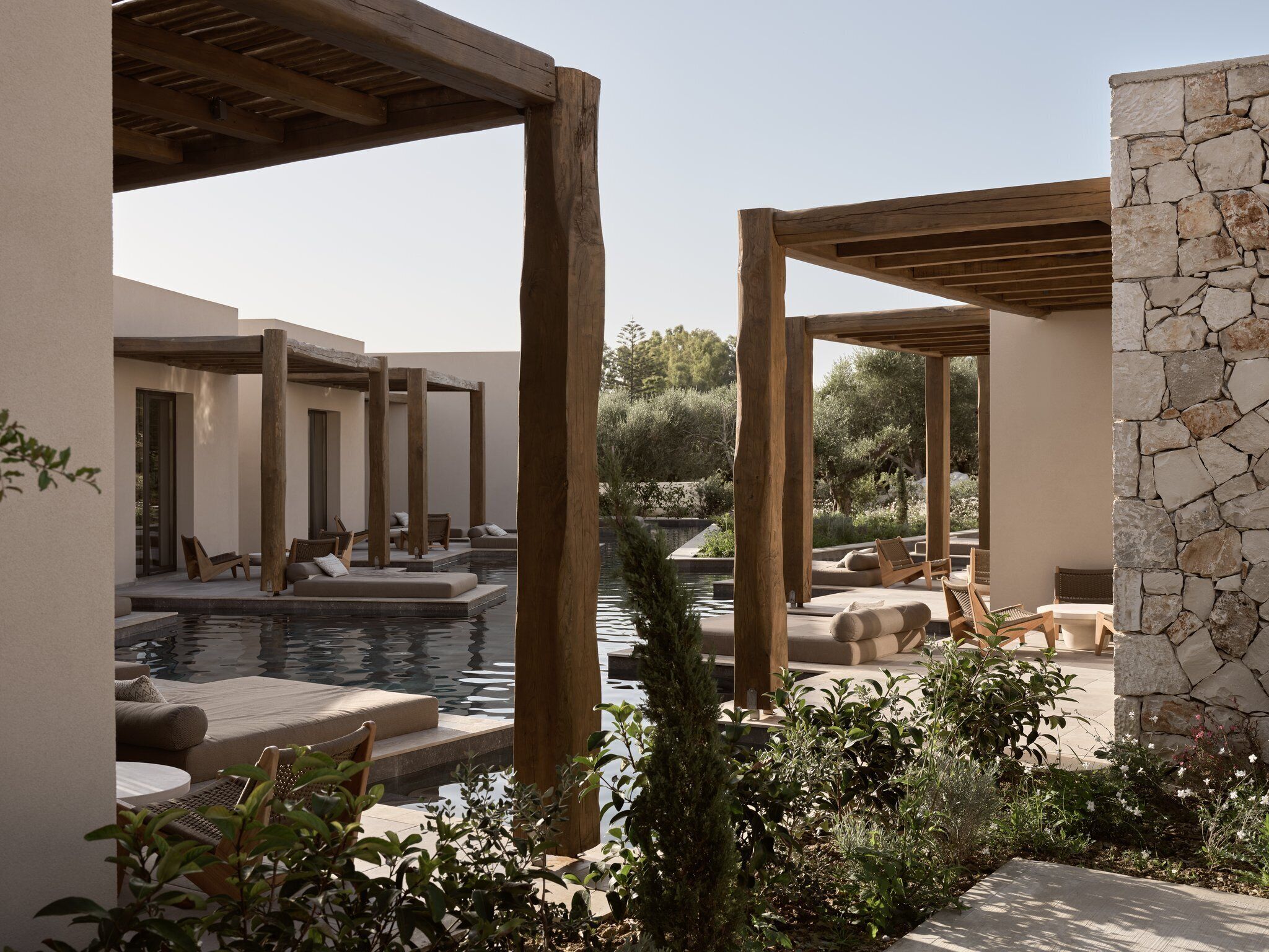 Zona de piscina con pérgolas de madera, muros de piedra y mobiliario exterior.
