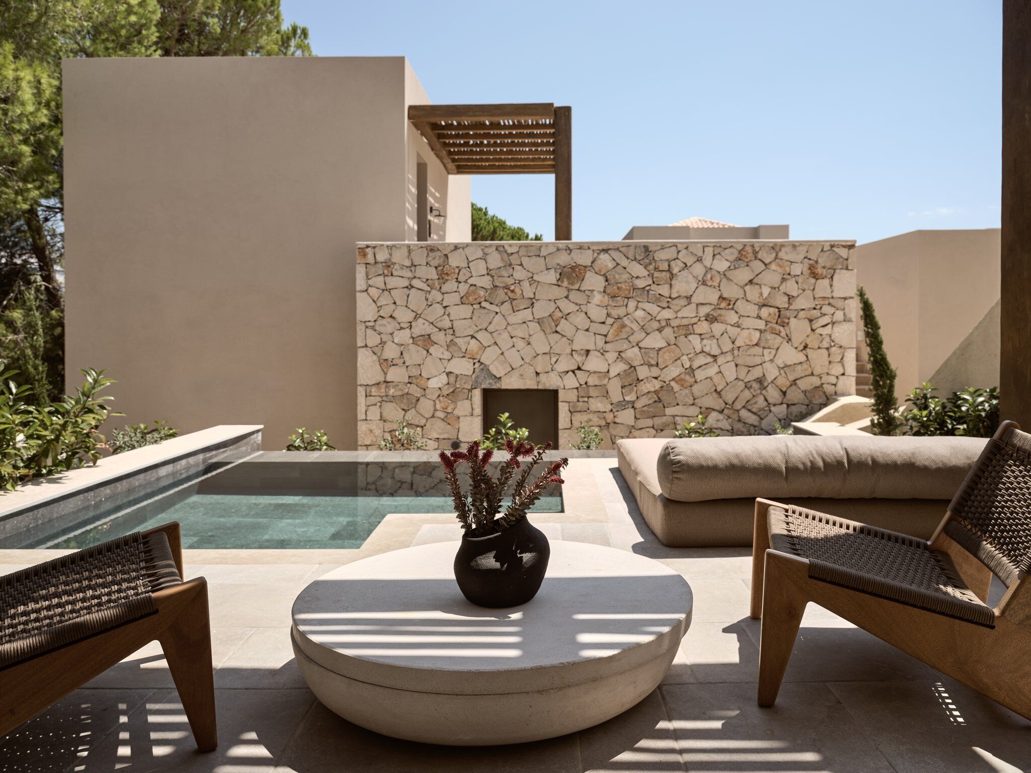 Un área junto a la piscina con un muro de piedra, una mesa redonda y dos sillas de mimbre.