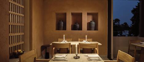 A dining area with a table set for two, wooden chairs, and a view of the outdoors at dusk.