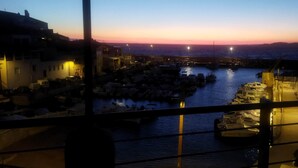 Vista sull'acqua con barche ormeggiate al molo, un tramonto sullo sfondo e edifici lungo le rive.