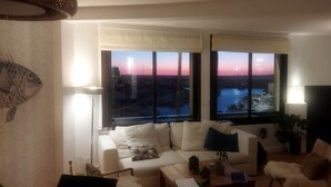 Un soggiorno con divano, tavolino e vista sul tramonto sull'acqua.