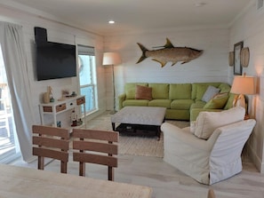 A living room with a green sofa, white armchairs, a wooden coffee table, and a fish wall decoration.