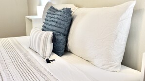 Ein Bett mit weißer Bettwäsche und zwei Kissen, eines gestreift, das andere mit fransigem Rand.