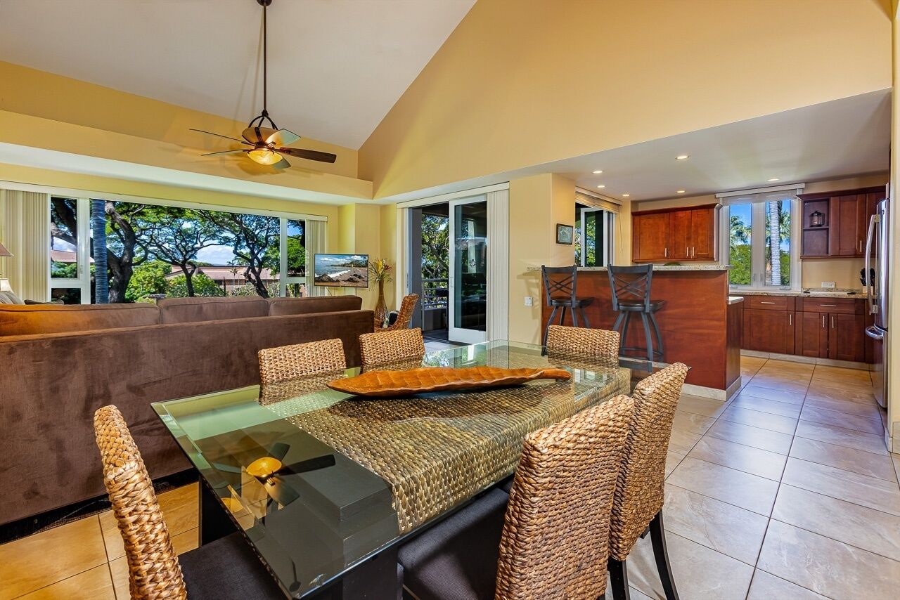 A modern dining area with a glass table, wicker chairs, and a sofa.