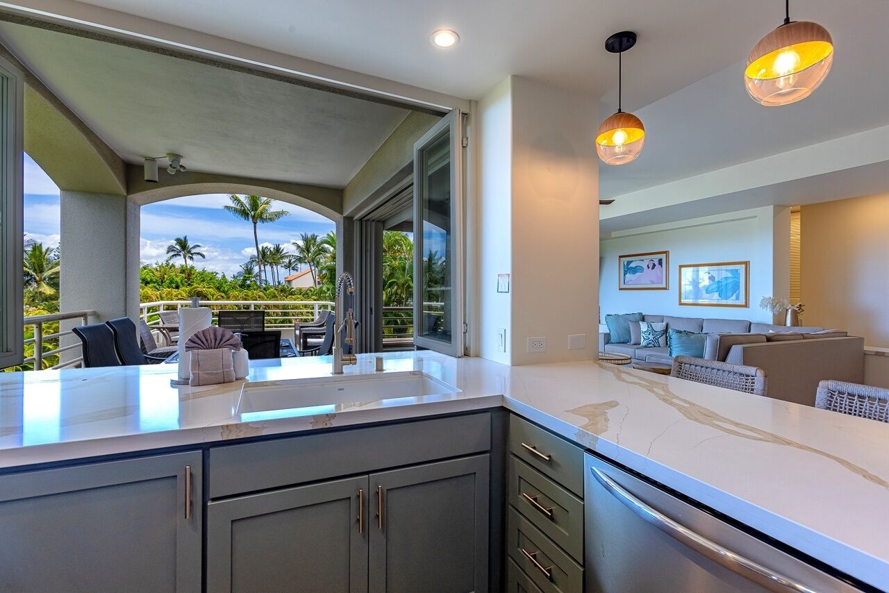 Una cocina moderna con una isla grande, un área de comedor con un sofá y vistas a palmeras y al océano.
