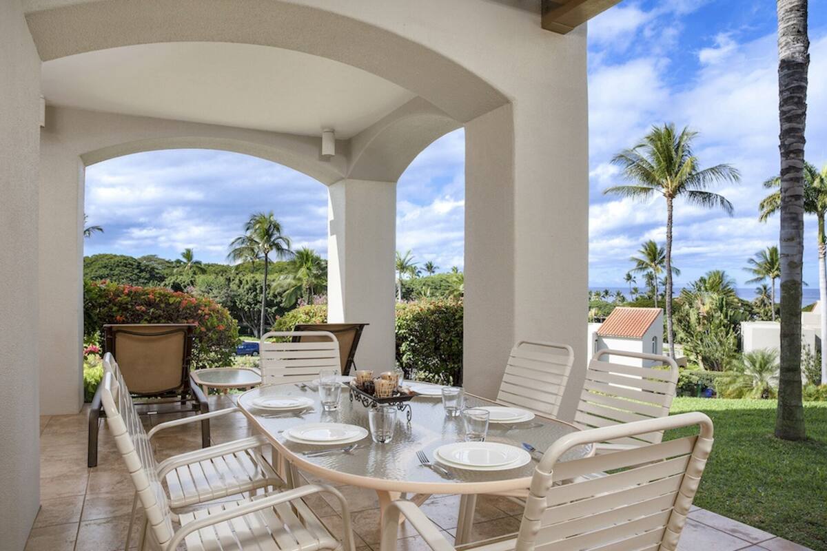A covered outdoor dining area with a table set for four, surrounded by white metal chairs, under a white ceiling with arches.