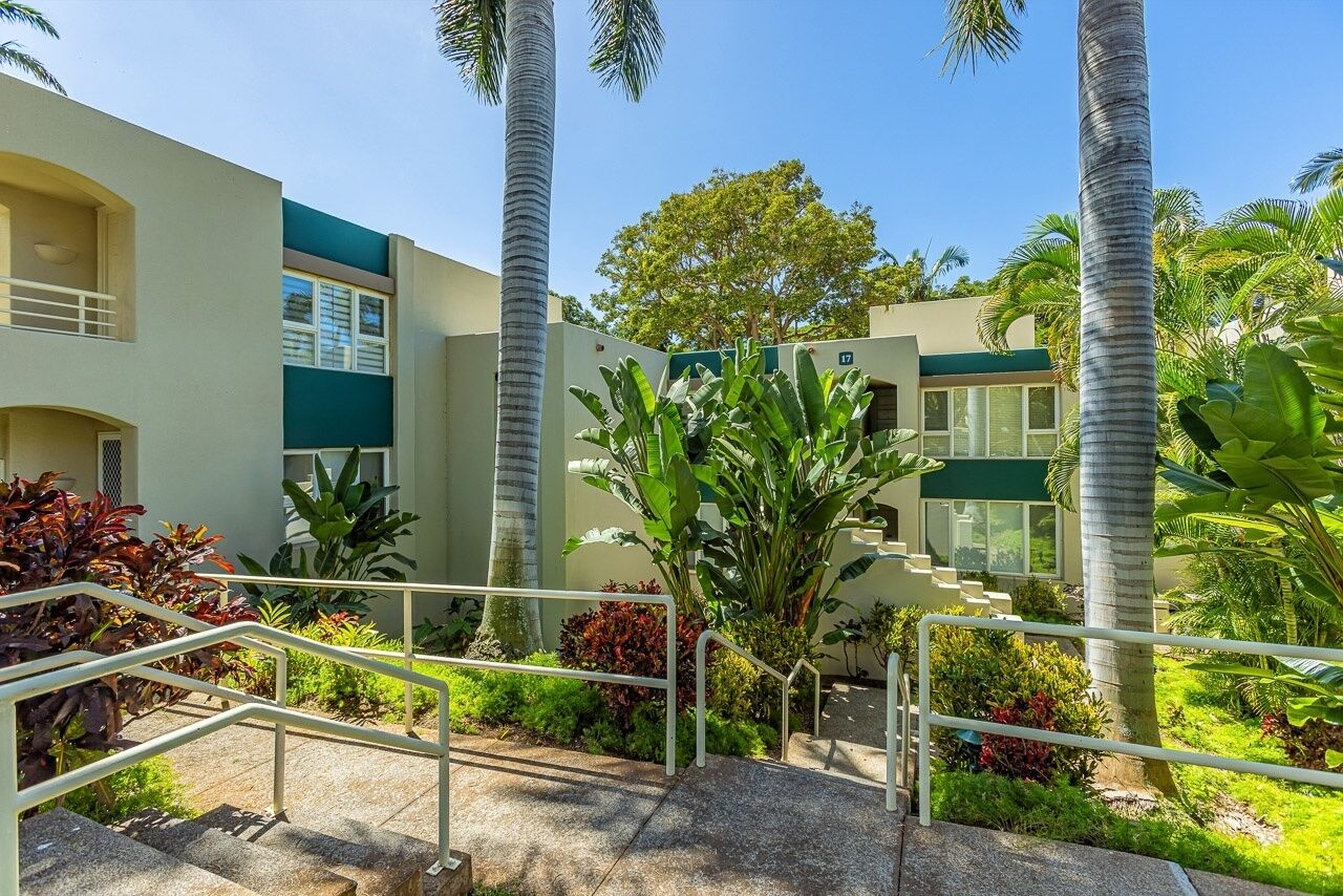 A modern building with a staircase, surrounded by lush greenery and palm trees.