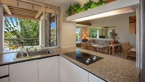 A modern kitchen with a built-in stove, a sink, and a window with a view of palm trees. - Palms at Wailea Two Bedrooms - Partial Ocean View by Coldwell Banker Island Vacations (Kihei)