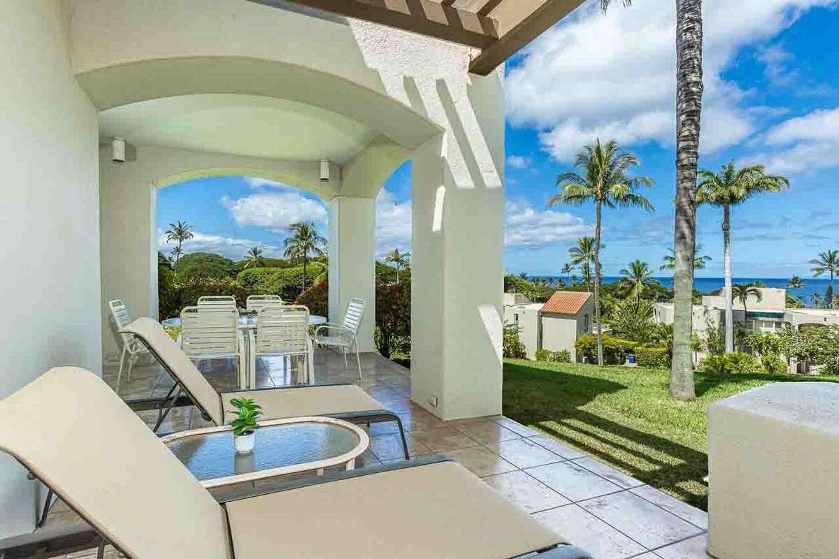 An outdoor patio with a pool table, lounge chairs, and a view of the ocean and palm trees.