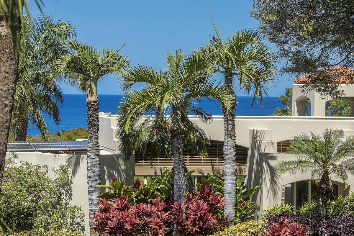 A resort with palm trees, a view of the ocean, and a building with a white facade.