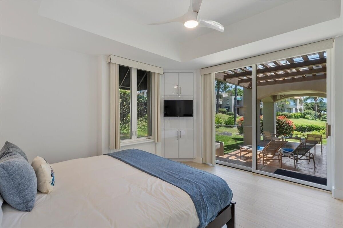 Une chambre à coucher comprenant un lit, un téléviseur et une porte-fenêtre coulissante donnant sur une terrasse aménagée avec du mobilier d’extérieur.