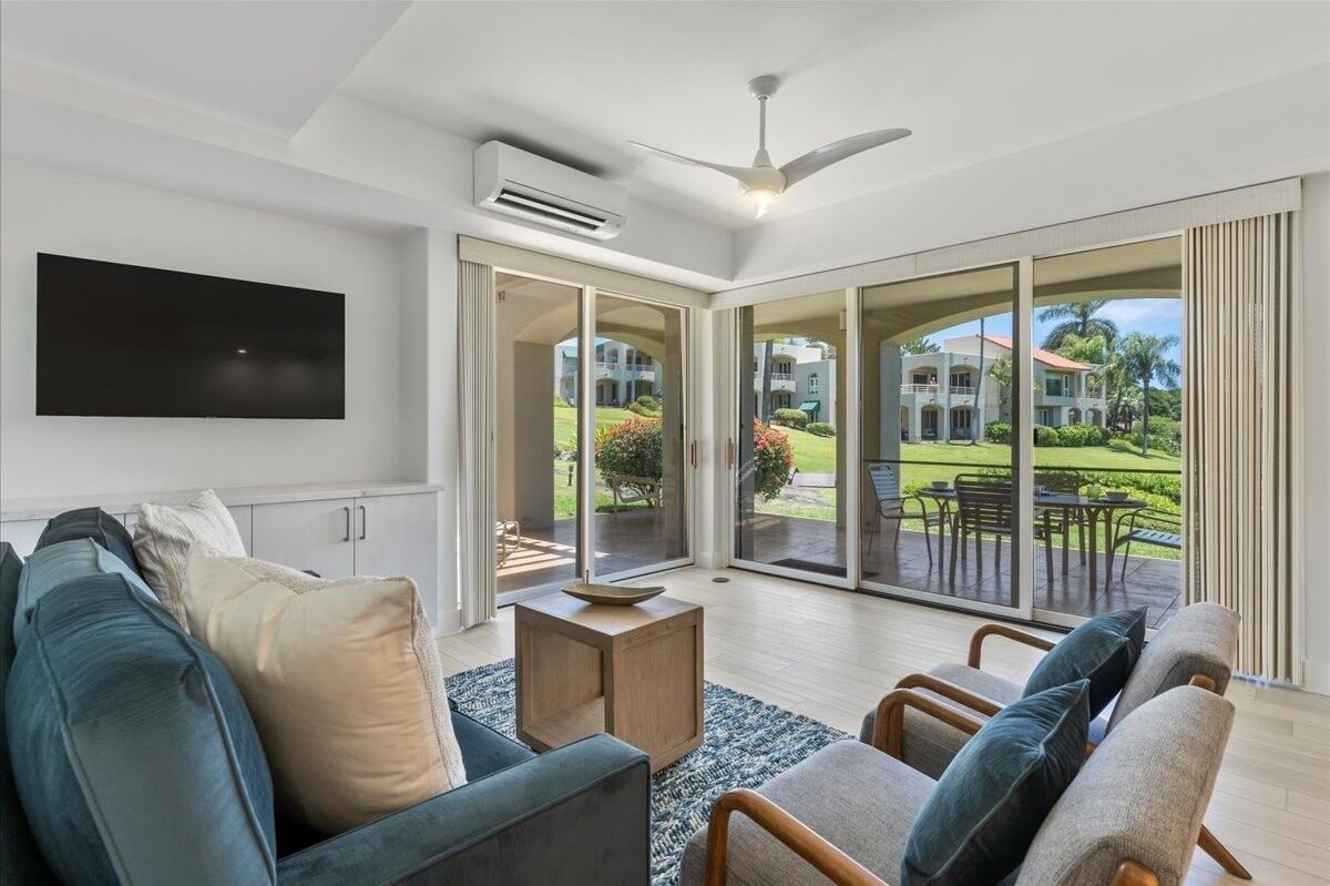 A modern living room with a flat-screen TV, a ceiling fan, and a large sliding glass door leading to an outdoor patio.