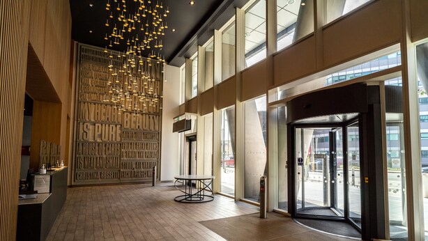 A spacious lobby with a modern design, featuring a reception desk, a wall with text, and a large glass door leading outside. - Luxury 2-bed Croydon Apartment Near Gatwick (Croydon)