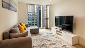 A modern living room with a large flat-screen TV, a grey sofa with yellow cushions, a fluffy rug, and a large window offering a city view. - Luxury 2-bed Croydon Apartment Near Gatwick (Croydon)