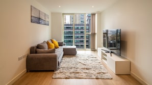 A modern living room with a sofa, a flat-screen TV, and a large window offering a city view. - Luxury 2-bed Croydon Apartment Near Gatwick (Croydon)