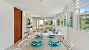Un coin repas avec une table dressée pour quatre personnes, des chaises blanches et une vue sur l’extérieur grâce à de grandes fenêtres.