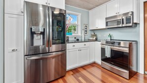 A modern kitchen with stainless steel appliances, white cabinetry, and a wooden floor.