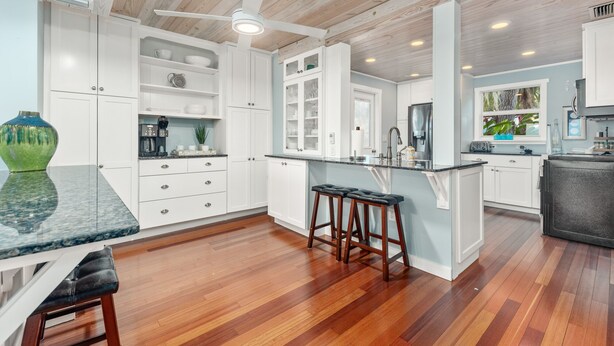 A modern kitchen with white cabinetry, a marble countertop, and a wooden ceiling.