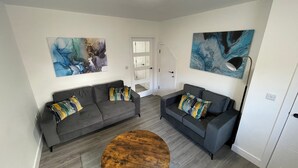 A modern living room with two grey sofas, a wooden coffee table, and abstract paintings on the walls. - Brand New High Spec House with parking (Newcastle-Under-Lyme)