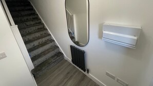 A staircase with carpeted steps, a wall-mounted radiator, and a large mirror. - Brand New High Spec House with parking (Newcastle-Under-Lyme)