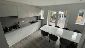 A modern kitchen with white cabinets, a black sink, and a dining area with a white table and four chairs. - Brand New High Spec House with parking (Newcastle-Under-Lyme)