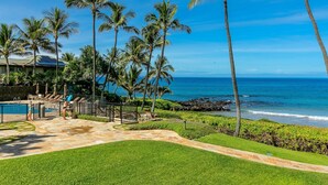 A pool area with lounge chairs and umbrellas, surrounded by palm trees and a view of the ocean. - Polo Beach Club Two Bedrooms - Sleeps 6 by Coldwell Banker Island Vacations (Kihei)