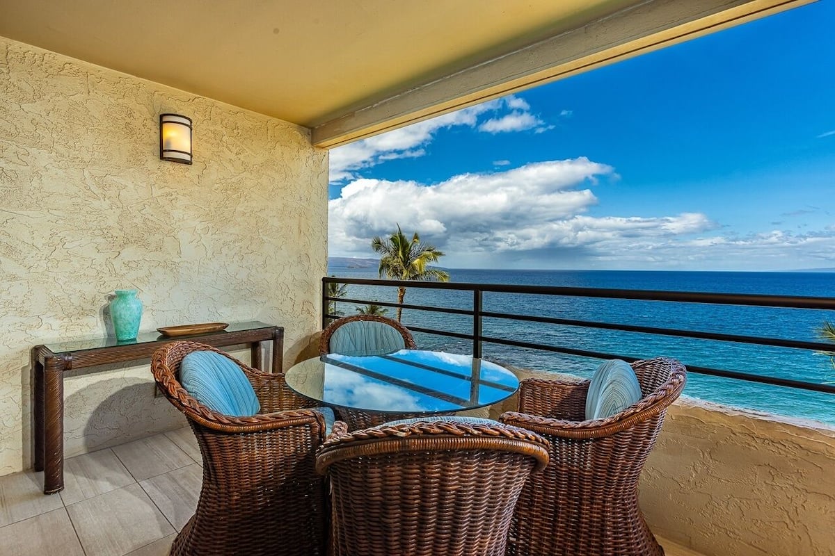 En balkon med fletmøbler, et glasbord og udsigt over havet.