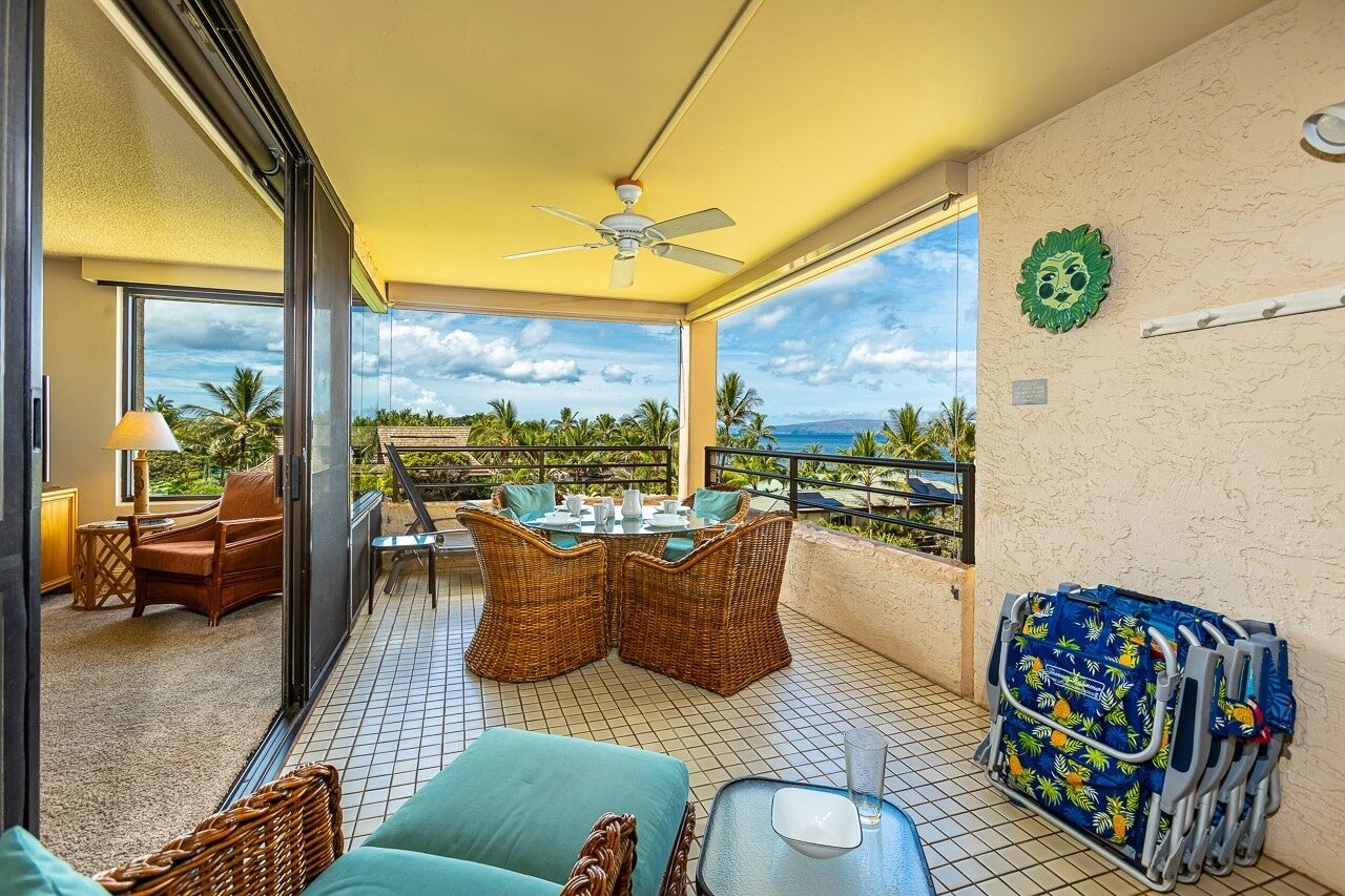 A balcony with wicker furniture, a table set for dining, and a view of the ocean.