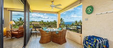 A balcony with wicker furniture, a table set for dining, and a view of the ocean.