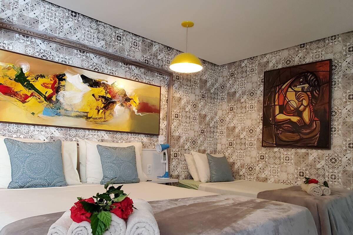 A hotel room with a bed, two bedside tables, a large abstract painting, a smaller artwork, and a decorative wall pattern.