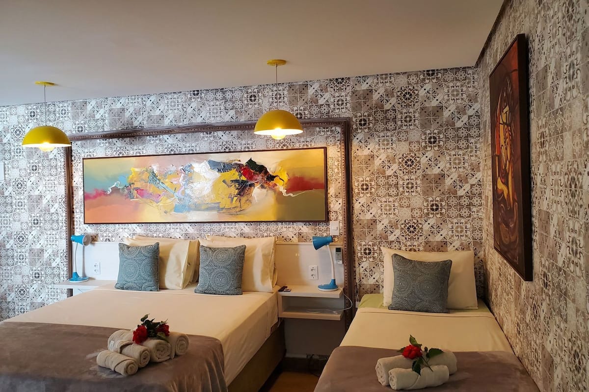 A hotel room with two beds, a large abstract painting, patterned wallpaper, and a nightstand with a lamp.