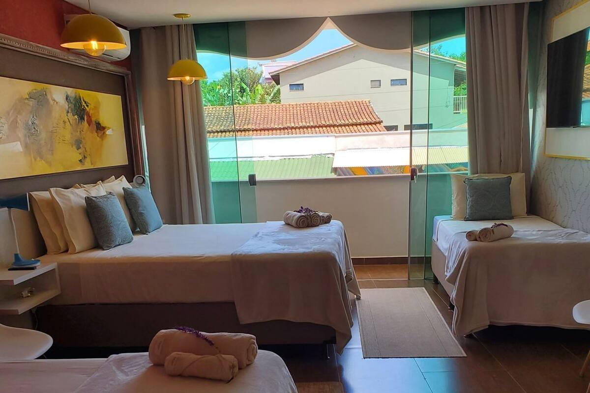 A hotel room with two beds, a large window, and a painting on the wall.