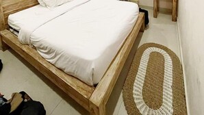 A bedroom with a wooden bed, a small wooden stool, a round woven rug, and a wall-mounted air conditioning unit. - A-Manta Homestay (Labuan Bajo)