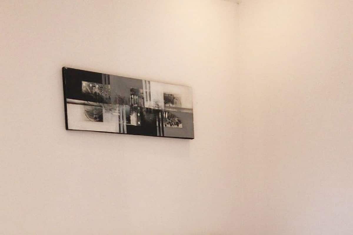 Un lit simple avec une literie blanche, dans une pièce aux murs unis et ornée d’un petit cadre.