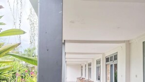 A covered outdoor area with rows of wooden chairs, a grassy garden, and a white building with large windows. - A-Manta Homestay (Labuan Bajo)