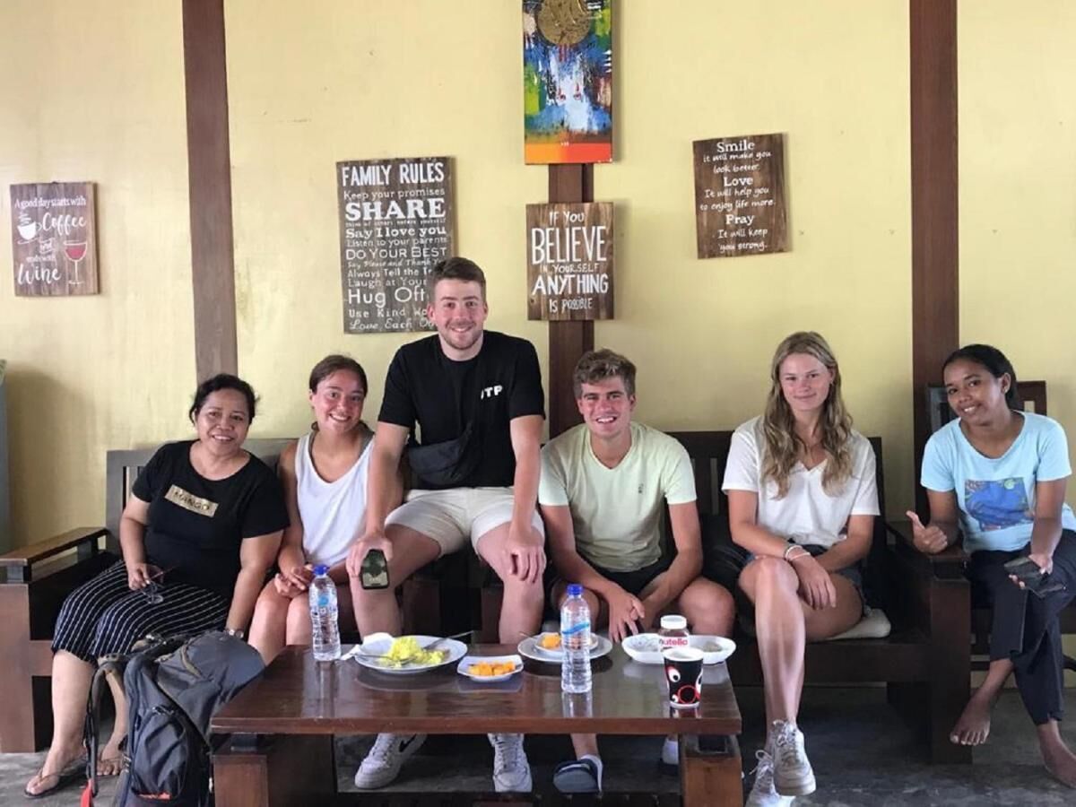 A group of people seated on a bench with a table in front of them. There are various signs on the wall behind them, including one that says "Family Rules Share Say I love you Do your best Always tell the truth Hug Off Use Kind Words Love Pray".