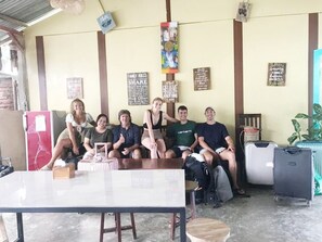 Un grupo de personas sentadas en una habitación con una mesa, sillas y varias decoraciones en las paredes.