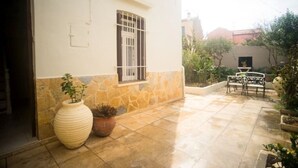 Un cortile con un muro in pietra, una finestra con inferriate, una pianta in vaso e una panchina.