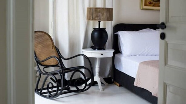 Una camera da letto con un letto, una sedia, un tavolino con una lampada e un quadro appeso al muro.