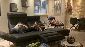Ein modernes Wohnzimmer mit einer schwarzen Ledersofa, zwei runden schwarzen Couchtischen und einer Wand mit Steinverkleidung.